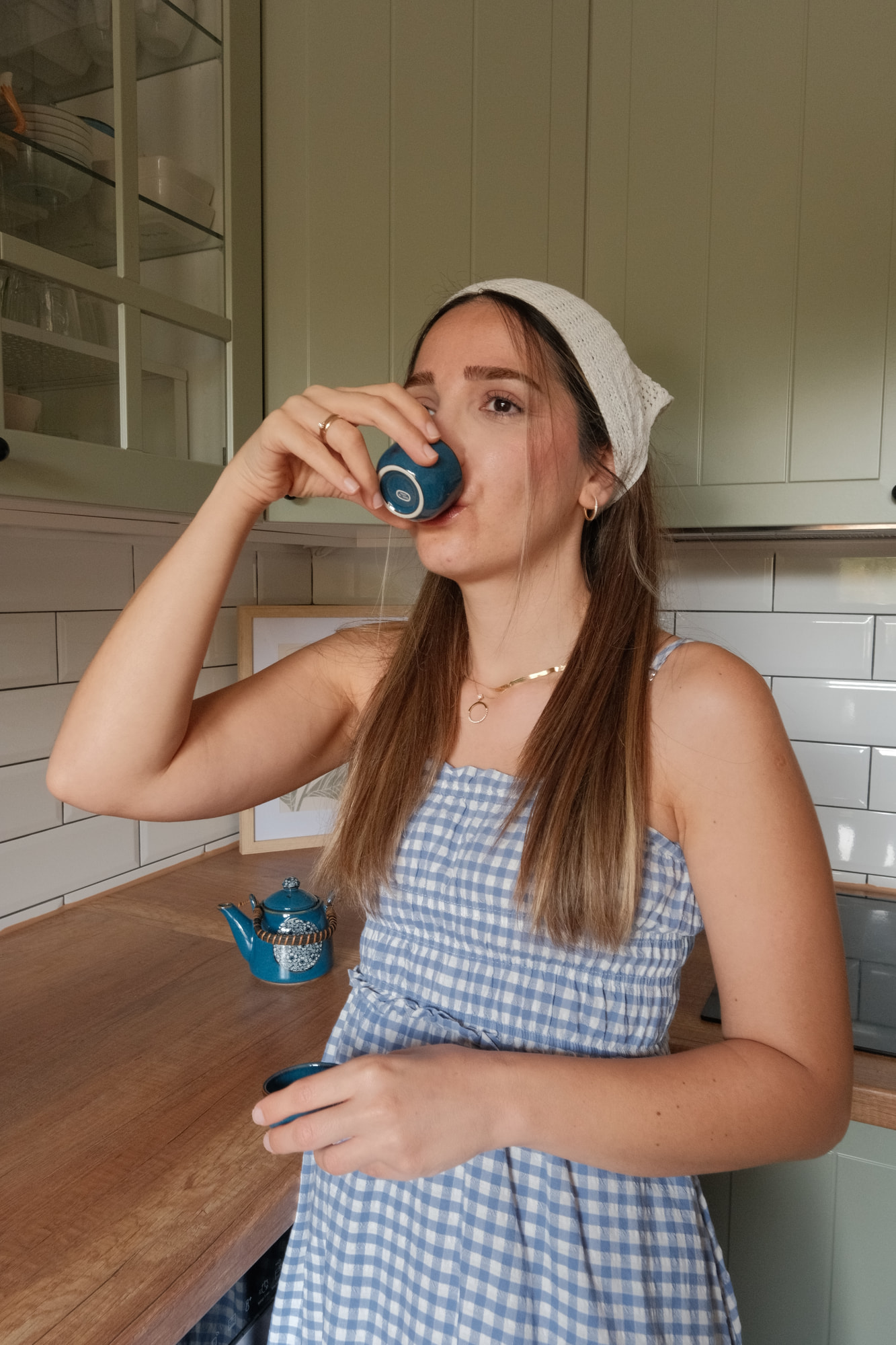 Elif Çimen Güngör trinkt in der Küche aus einer kleinen petrolfarbenen Tasse, auf der Holzarbeitsplatte steht die passende Teekanne.