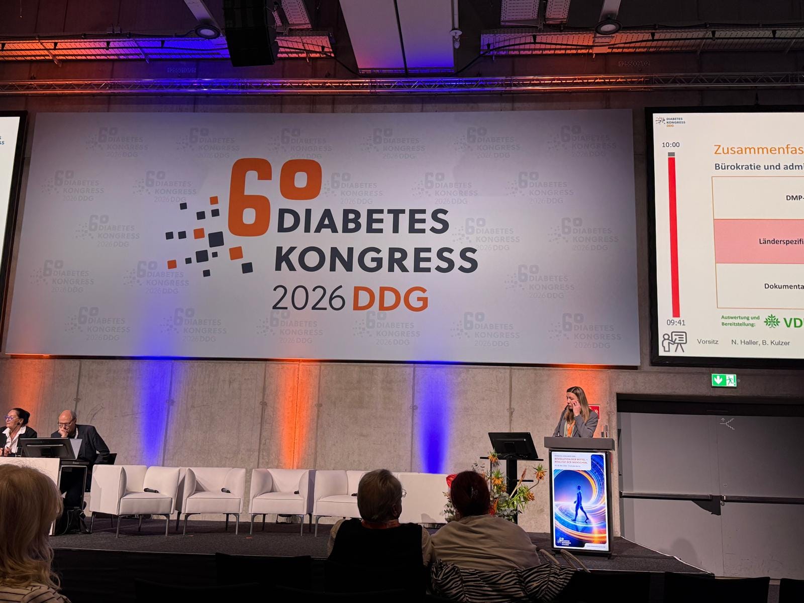 Bühne beim 60. Diabetes Kongress der DDG 2026: großes Kongresslogo, daneben eine Präsentationsfolie, eine Referentin am Rednerpult und Zuhörende im Vordergrund.